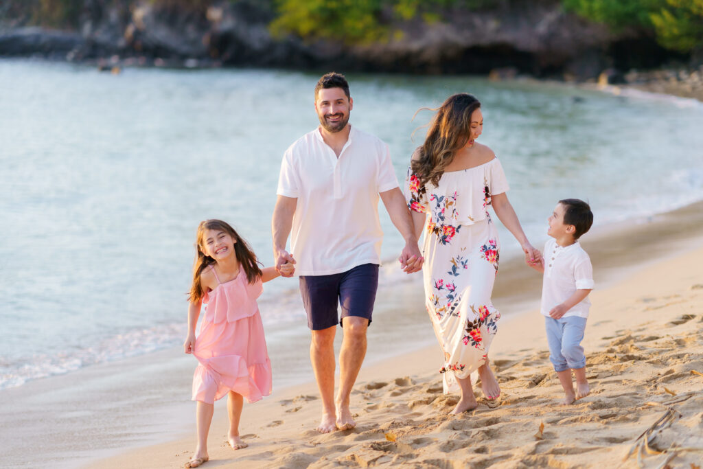 Family walking along Kapalua Bay beach, Maui, in coordinated pastel outfits, enjoying a relaxed photo session.