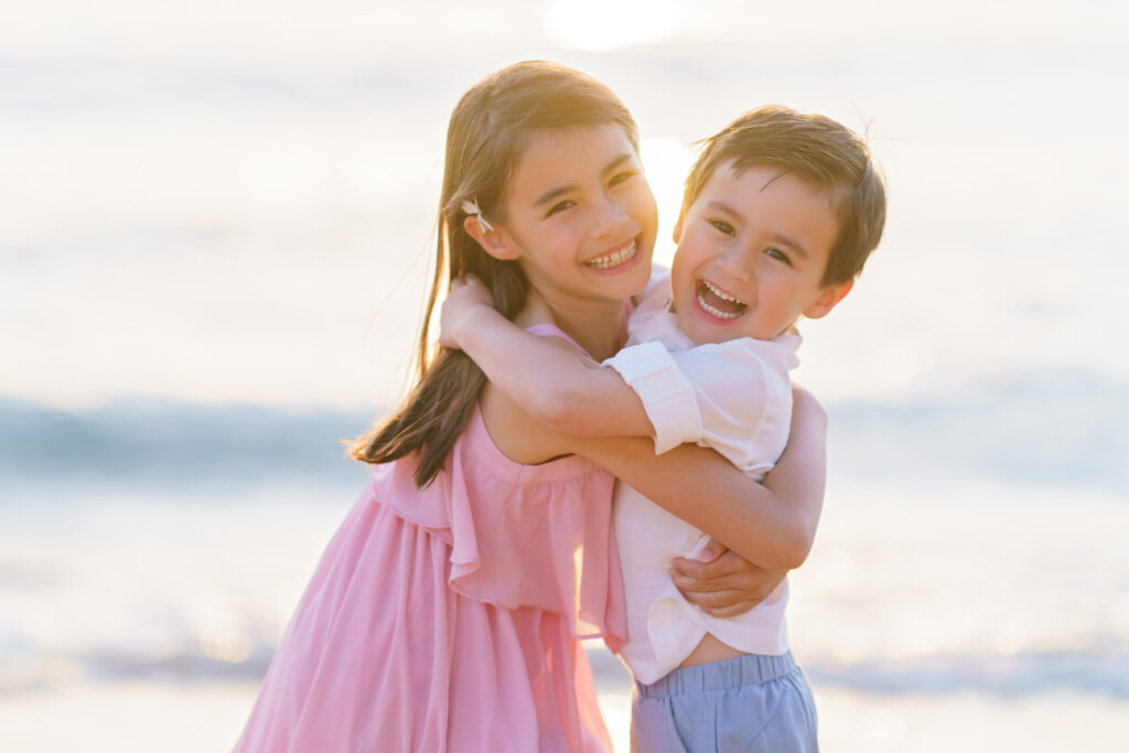 Siblings sharing a sweet hug at sunset on Kapalua Bay beach, Maui, during a family photo session.