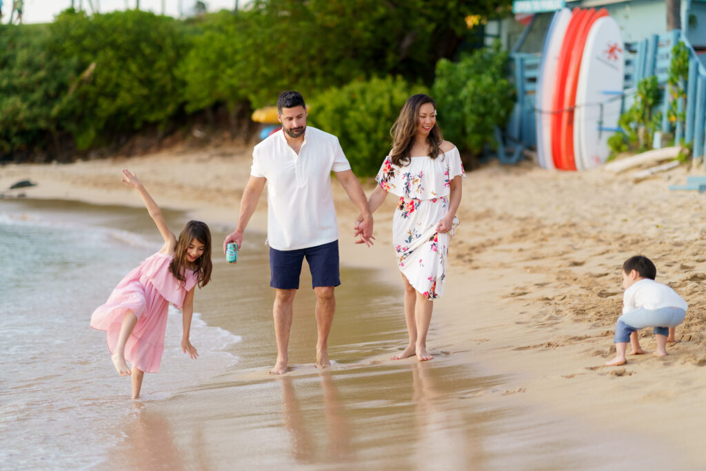 Family enjoying the shoreline at Kapalua Bay, Maui, with vibrant surfboards and palm trees in the background."