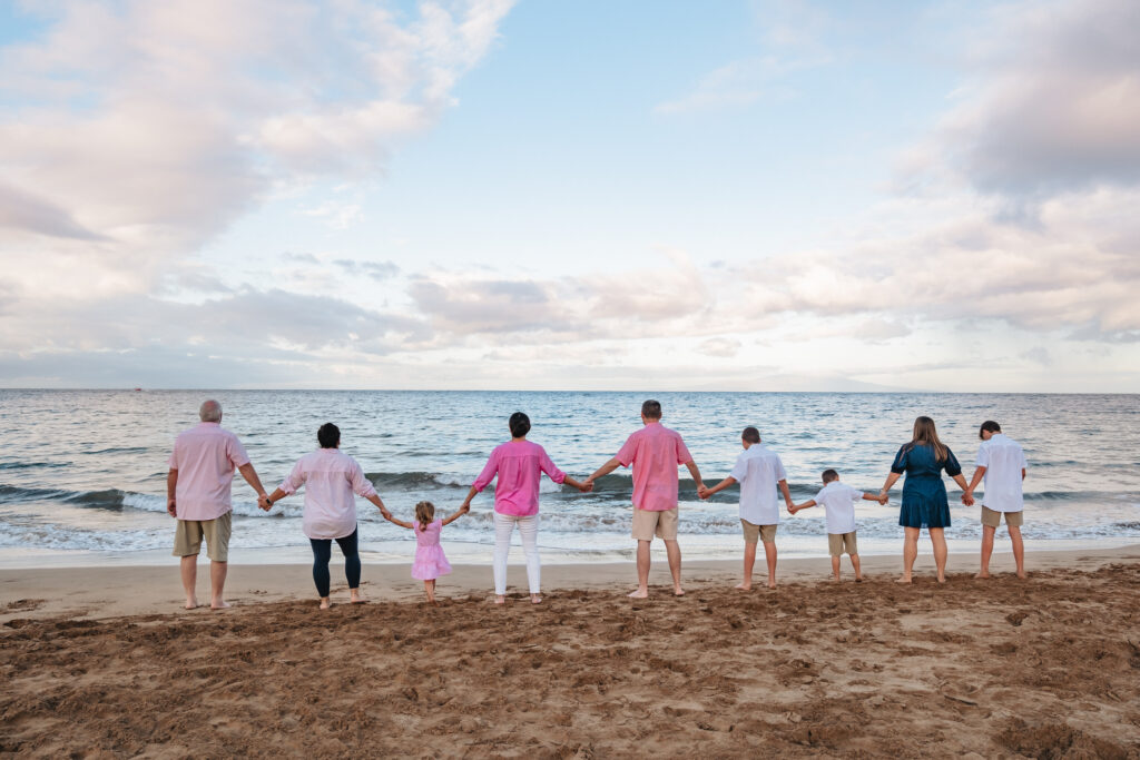 Family members hold hands while walking along the shoreline at sunrise family session in Maui.
