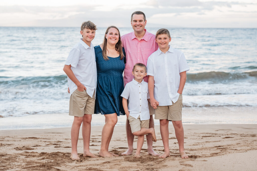 A family of five smiles for the camera, waves gently touching the sand behind them.