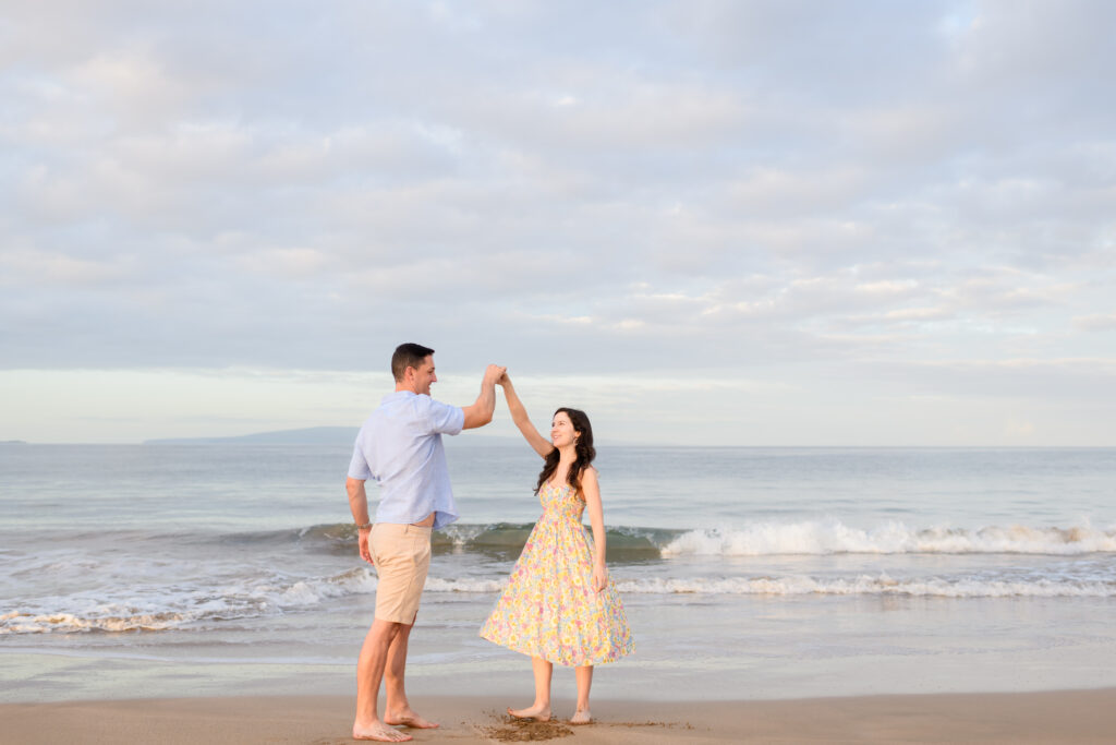 A joyful couple dances on a serene Maui beach, with gentle waves and a pastel sky creating a romantic backdrop—perfectly